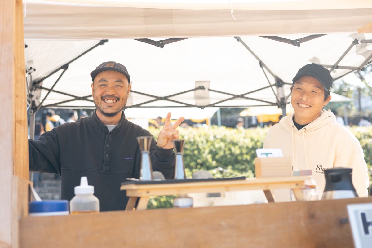 コーヒー器具が並ぶブースで笑顔を見せる二人の出店者