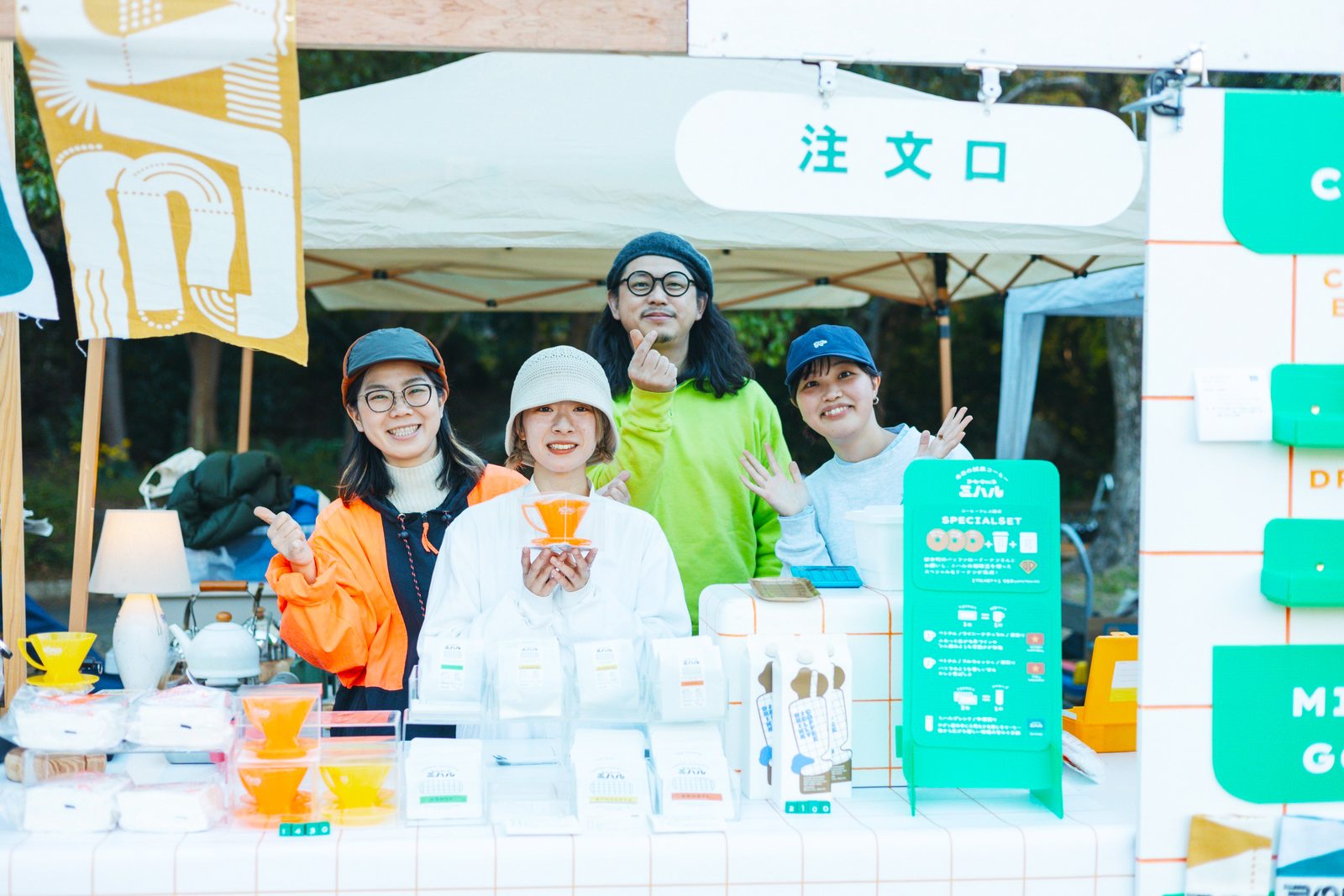 色鮮やかなコーヒー器具が並ぶブースでポーズをとる四人の出店者
