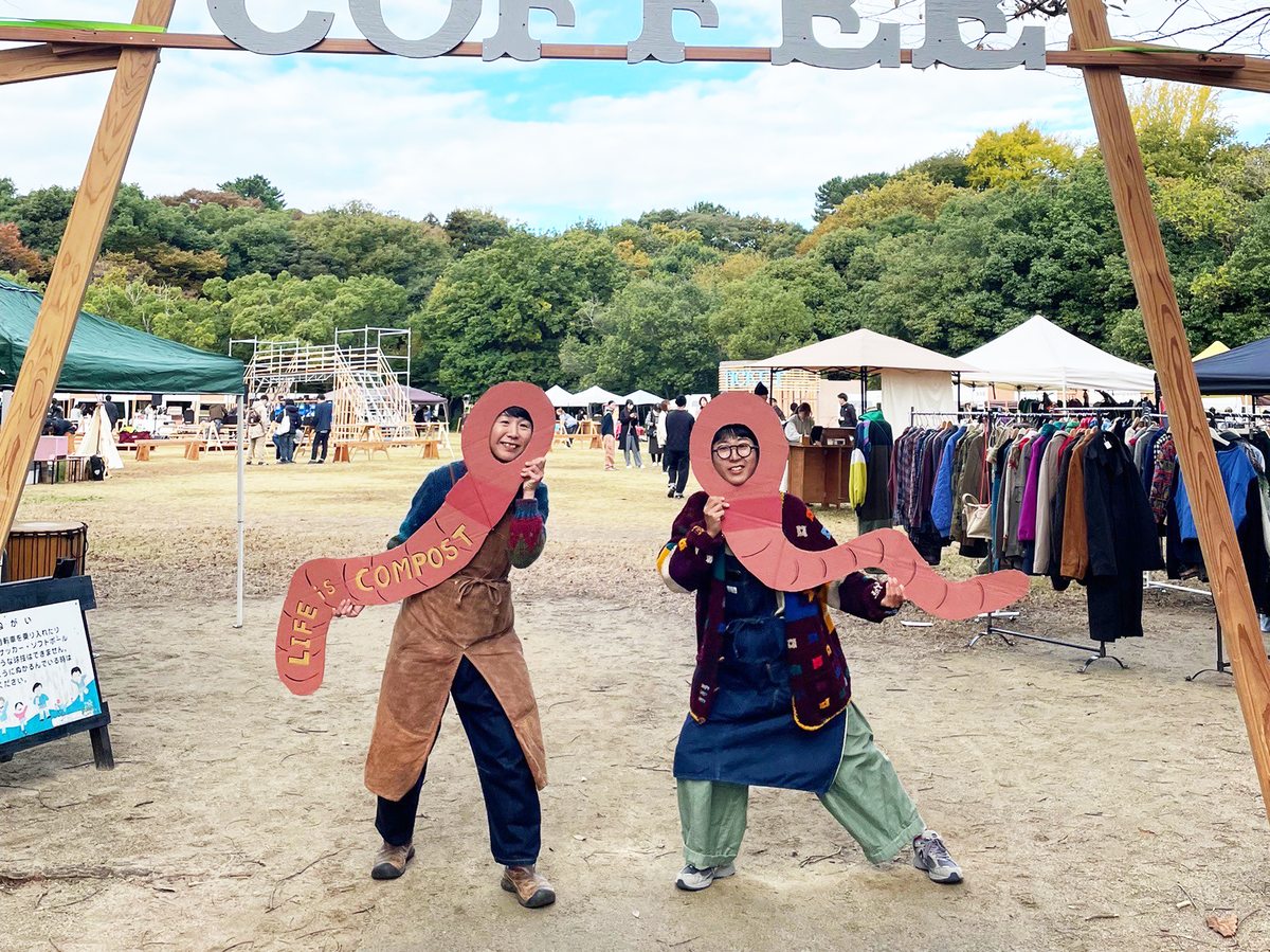 会場の入口でミミズ型のパネルを持ってポーズをとる二人