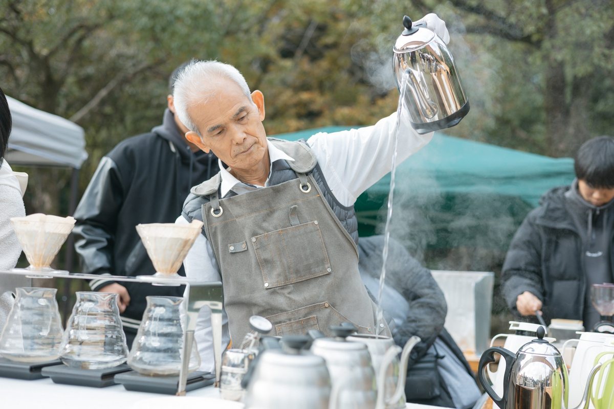 屋外のコーヒーブースで、ケトルからお湯を注ぐ出店者